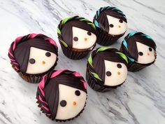 six cupcakes with chocolate frosting decorated to look like women's faces