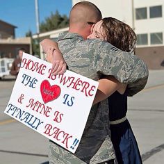 a man and woman hug each other while holding a sign that says home is where the us and mine is finally back