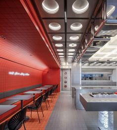 the interior of a restaurant with red walls and ceiling lights hanging from the ceiling, along with long tables and chairs