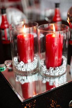 two red candles are sitting in glass cups on a table with silverware and other decorations