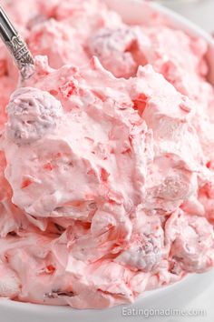 a white bowl filled with pink frosting next to a spoon