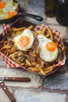 two fried eggs on top of french fries in a basket with red and white checkered paper