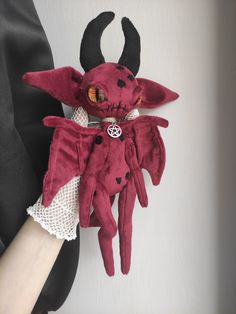 a red stuffed animal with horns on it's head is being held by someone