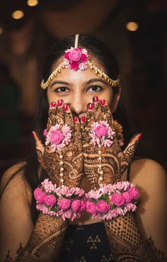 a woman with her hands covered in henna and pink flowers on her face, looking at the camera