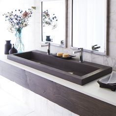 a bathroom sink sitting under two mirrors in front of a vase with flowers on it