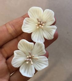 two white flowers sitting on top of each other in someone's hand with their fingers