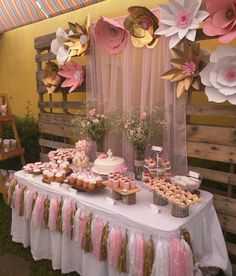 a table topped with cupcakes and cakes next to a pink flower covered wall