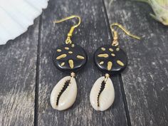 "These gorgeous dangle earrings feature genuine off-white sliced moneta cowrie shells dangling beneath 20mm round carved black and gold acrylic beads an etched Afrocentric abstract pattern. Aching for acrylics? Check out the rest of my acrylic jewelry here: https://etsy.me/2IadiWZ Throughout Africa and the Americas, cowrie shells have historically been viewed as symbols of womanhood, fertility, and prosperity. Check out my other cowrie shell jewelry here: https://etsy.me/2VQS0r0 These earrings m Artisan Black Jewelry For The Beach, Handmade Black Earrings For Beach, Black Dangle Jewelry For Beach, Black Shell Jewelry For Gifts, Black Shell Jewelry Gift, Black Shell Jewelry As A Gift, Handmade Black Jewelry For Vacation, Cowrie Shell Earrings For Gifts, Handmade Black Jewelry For Beach