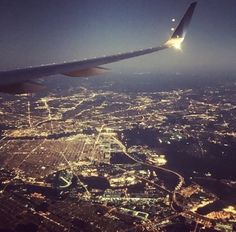 the wing of an airplane flying over a city at night with lights on it's sides