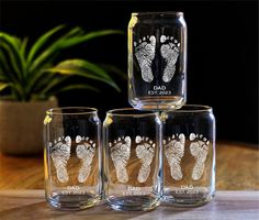 three glass tumblers with baby footprints on them sitting on a table next to a potted plant