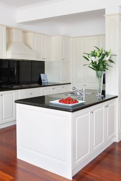 a kitchen with white cabinets and black counter tops, an island in the middle has a bowl of strawberries on it