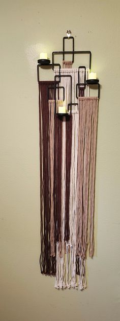 a wall hanging with three candles and fringes on it's sides in front of a white wall