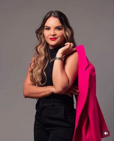 a woman with long hair wearing black pants and a pink jacket is posing for the camera