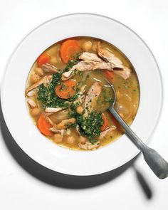 a bowl of soup with chicken, carrots and broccoli on a white plate