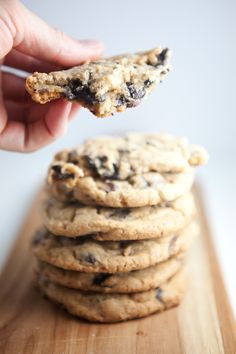 a hand holding a cookie over a stack of cookies