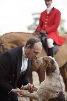 a man in a tuxedo petting a brown and white dog on the nose