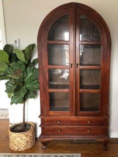 a wooden cabinet sitting next to a potted plant on top of a hard wood floor