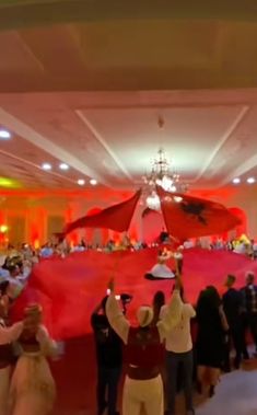 a large group of people standing in a room with red cloths on the ceiling