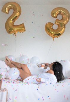 a woman laying on a bed with balloons and confetti