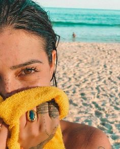 a woman covers her face with a towel on the beach while looking at the camera