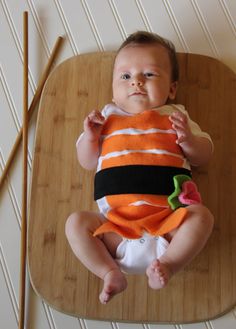 a baby wearing an orange and black outfit sitting on top of a wooden table next to chopsticks