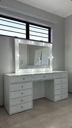 a white vanity with lights on it in front of a large mirror and two windows