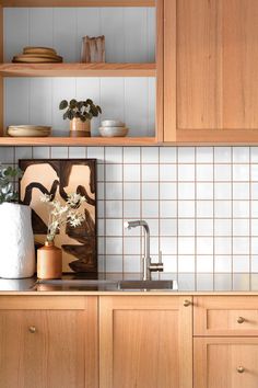 a kitchen with wooden cabinets and white tile backsplashing, an art work on the wall