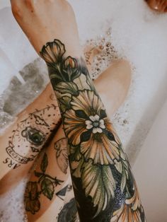 a woman's arm with flowers on it in the bathtub next to her legs