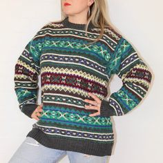 a woman standing in front of a white wall with her hands on her hips wearing a colorful sweater