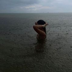 a woman is sitting in the water with her hands behind her head and looking out to sea