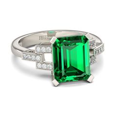 an emerald and diamond ring set in white gold with diamonds on the sides, surrounded by two