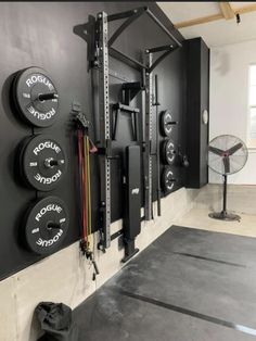 a home gym with black walls and white flooring is pictured in this image, there are several different types of equipment hanging on the wall