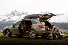 a man sitting on the ground next to a car with its trunk open and it's hatch opened