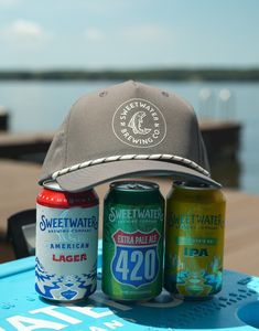 three cans of beer and a hat sitting on top of a surfboard