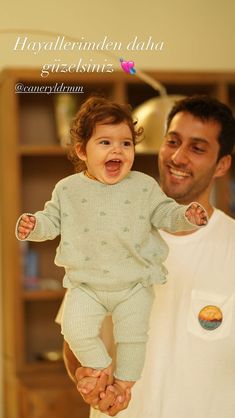 a man holding a baby in his arms and smiling at the camera while he holds it up