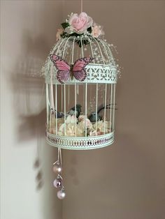 a white birdcage with pink flowers and butterflies hanging from it's sides