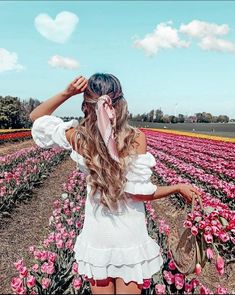 a woman with long hair standing in a field of tulips wearing a white dress