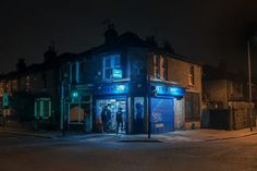 an empty street at night with people walking in the doorway and storefronts lit up