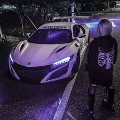 a woman standing next to a white car with skeleton on it's hoodie