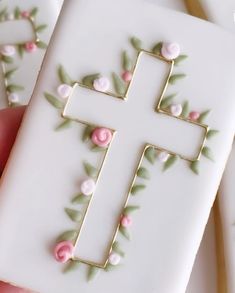 a cross decorated with pink flowers and green leaves on top of a white card holder