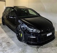 a black car parked in a garage next to a white wall and cement flooring