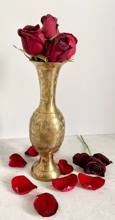 a gold vase filled with red roses sitting on top of a white table next to petals