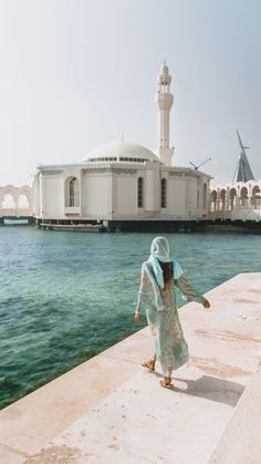 a woman walking along the edge of a body of water in front of a white building