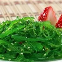 a white plate topped with green veggies and strawberries on top of a bamboo mat