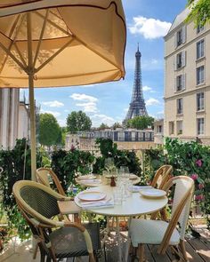 an outdoor table with chairs and umbrellas on a balcony overlooking the eiffel tower