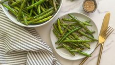 green beans and sesame seeds in bowls on a marble table with gold utensils