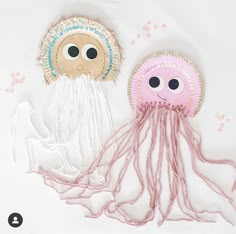 two jelly fish made out of paper plates on a white tablecloth with pink thread