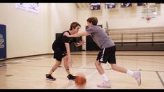 two young men playing basketball on an indoor court with one holding the ball in his hand