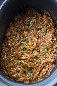 a slow cooker filled with shredded noodles and garnished with green parsley