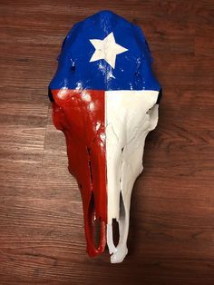 a cow skull with the colors of texas flag painted on it's side, sitting on a wooden surface